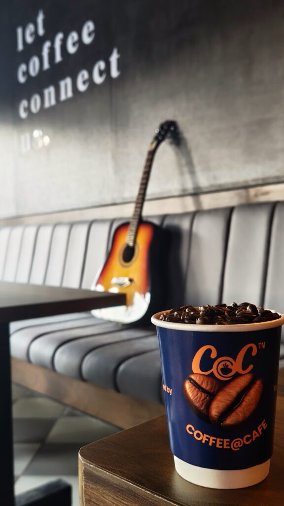 Coffee@Cafe cup filled with coffee beans, with a guitar behind it