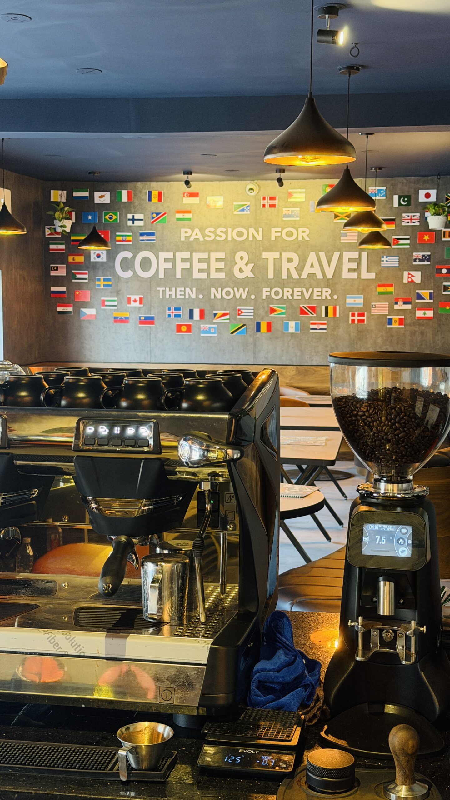 Espresso machine and grinder in front of a wall of flags reading passion for coffee and travel